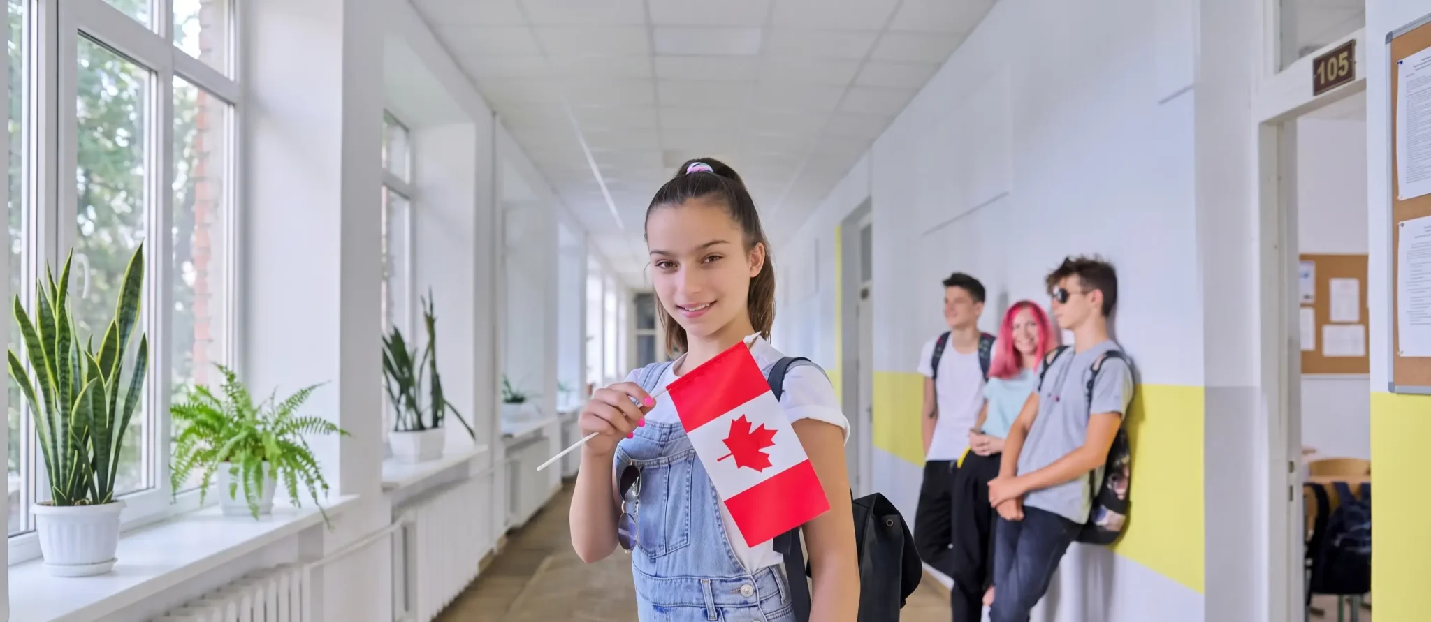 Joven estudiante sonriente sosteniendo una bandera de Canadá en el pasillo de un instituto durante su programa de año escolar en Canadá.