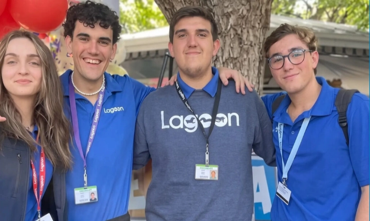 Cuatro jóvenes operadores de atracciones del parque Lagoon, con polos y una sudadera con el logo de 'Lagoon' y tarjetas de identificación, abrazándose y sonriendo.